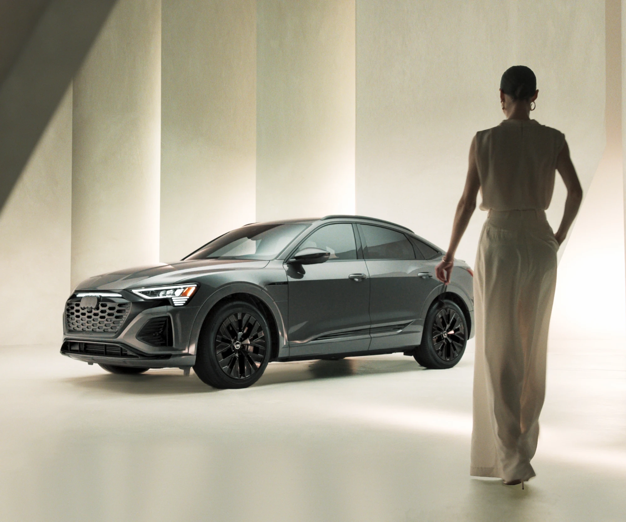 A dark gray Audi Q8 e-tron Sportback in a pale, softly lit studio of tall columns.