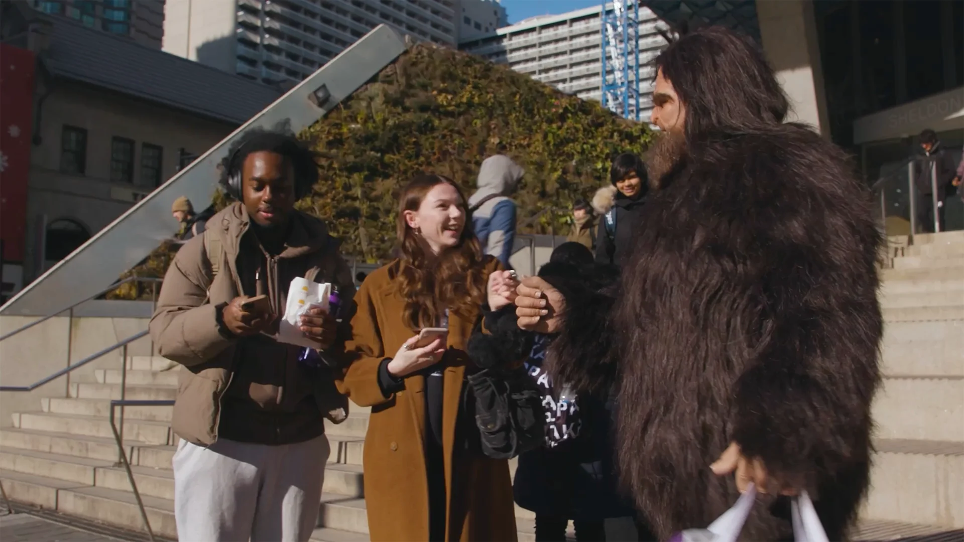 Sasquatch chats with laughing students on the steps of a downtown Toronto plaza.