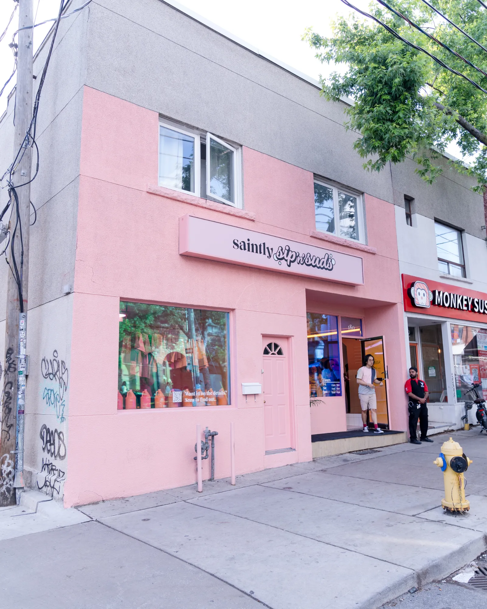 The Saintly Sip &rsquo;n&rsquo; Suds storefront: a two-storey building painted pink on a Toronto street, with a guest stepping out of the open door.
